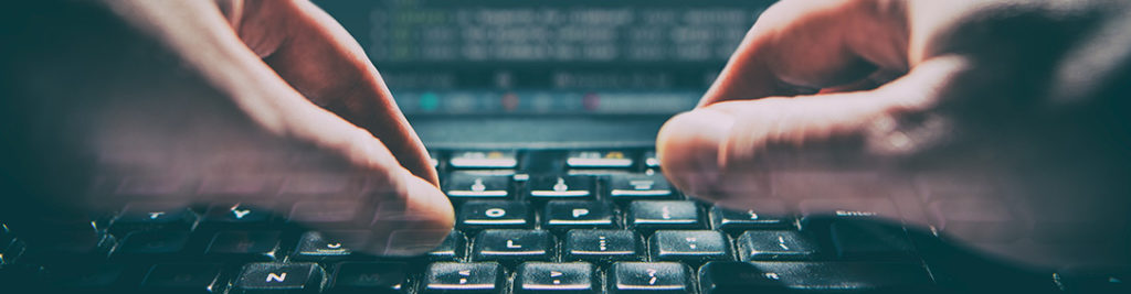 Close-up of hands typing quickly on a keyboard, with a computer screen displaying blurred text in the background, suggesting intense focus and fast-paced activity.